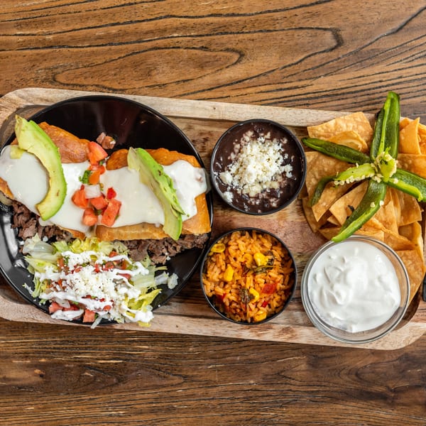 Mexican Mariachi Grill's carne asada with rice, beans, chips, salsa, and sour cream on a wooden tray.