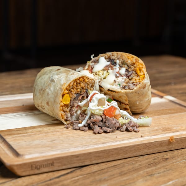 Two Mexican burritos, one cut open, revealing rice, meat, corn, and drizzled with white sauce.