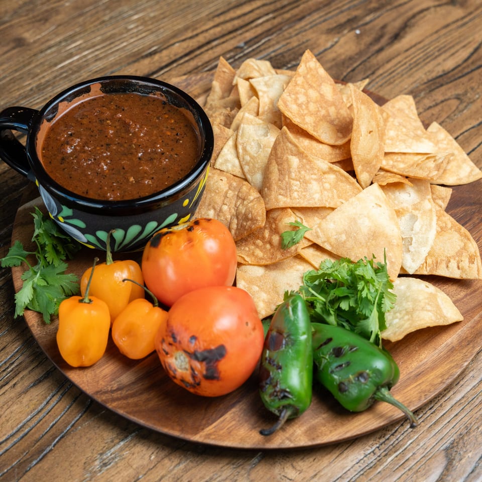 Mexican Mariachi Grill's salsa, tortilla chips, habanero peppers, tomatoes, and jalapeños on a wooden board.