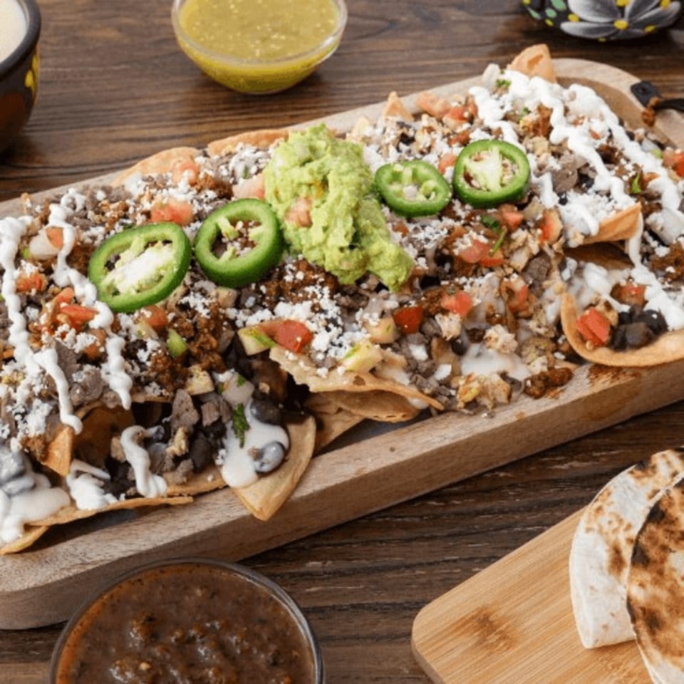 Loaded Mexican nachos with meat, beans, cheese, guacamole, sour cream, and jalapeños on a wooden board.