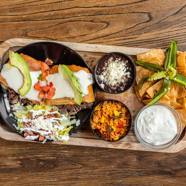 Mexican Mariachi Grill's steak fajita with avocado, rice, beans, chips, and sour cream on a wooden board.