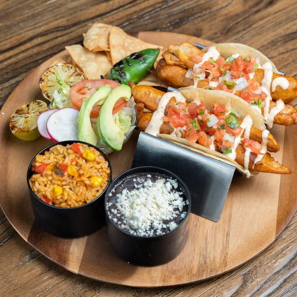 Mexican Mariachi Grill's fish tacos with rice, black beans, and a side salad on a wooden platter.